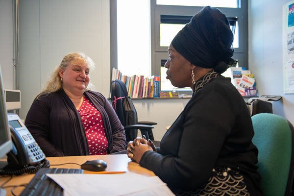 Two ladies sat around a desk in an office talking