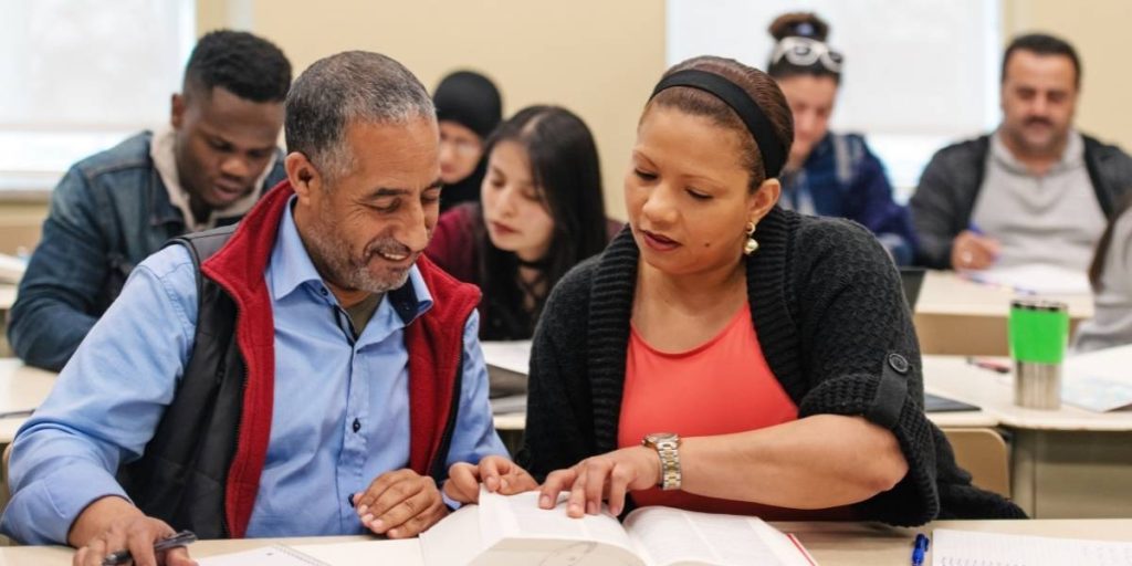 A woman and man sat in a classroom reading a book together