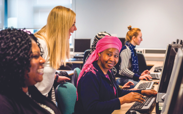 Several ladies on computers with a lady instructing them