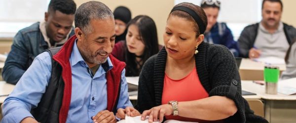 A woman and man sat in a classroom reading a book together