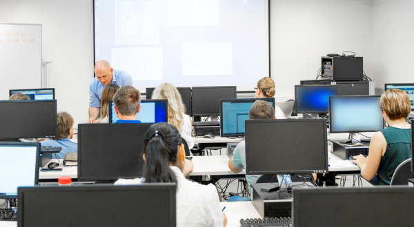 Interior of computer classroom with students being taught whilst sat around computers